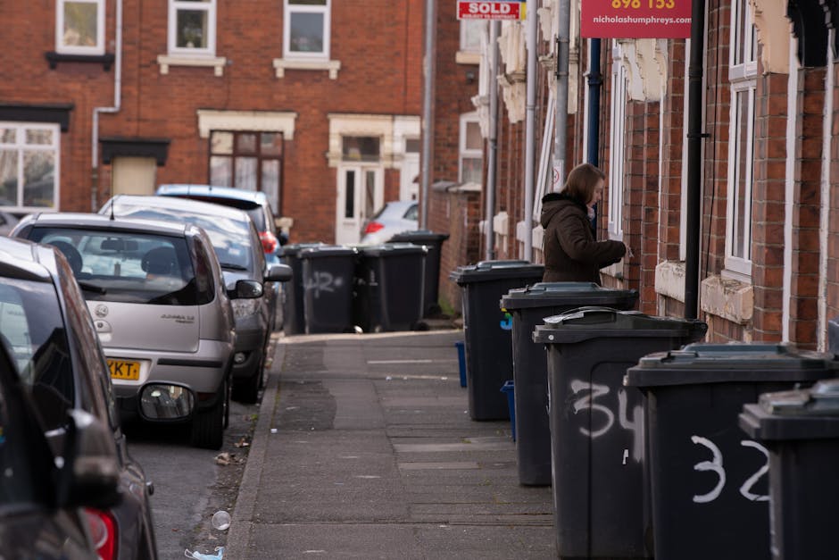 The image displays an outdoor area with a large collection of waste materials and recycling items arranged on a paved surface. Prominently, there are numerous stacks of empty fruit and vegetable boxes